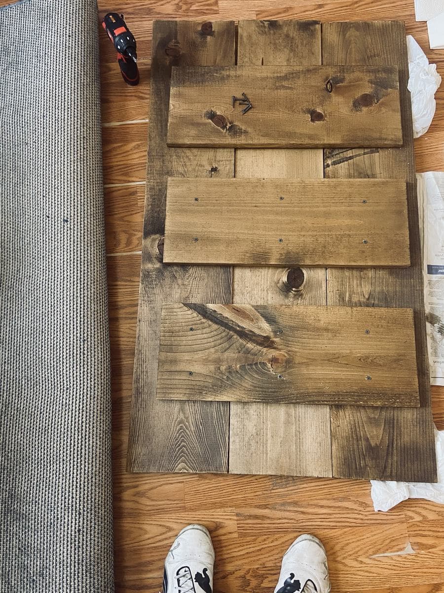 The tabletop face down, its three boards held together by three shorter boards screwed across the back. A cordless drill and a small pile of screws sit on the work.