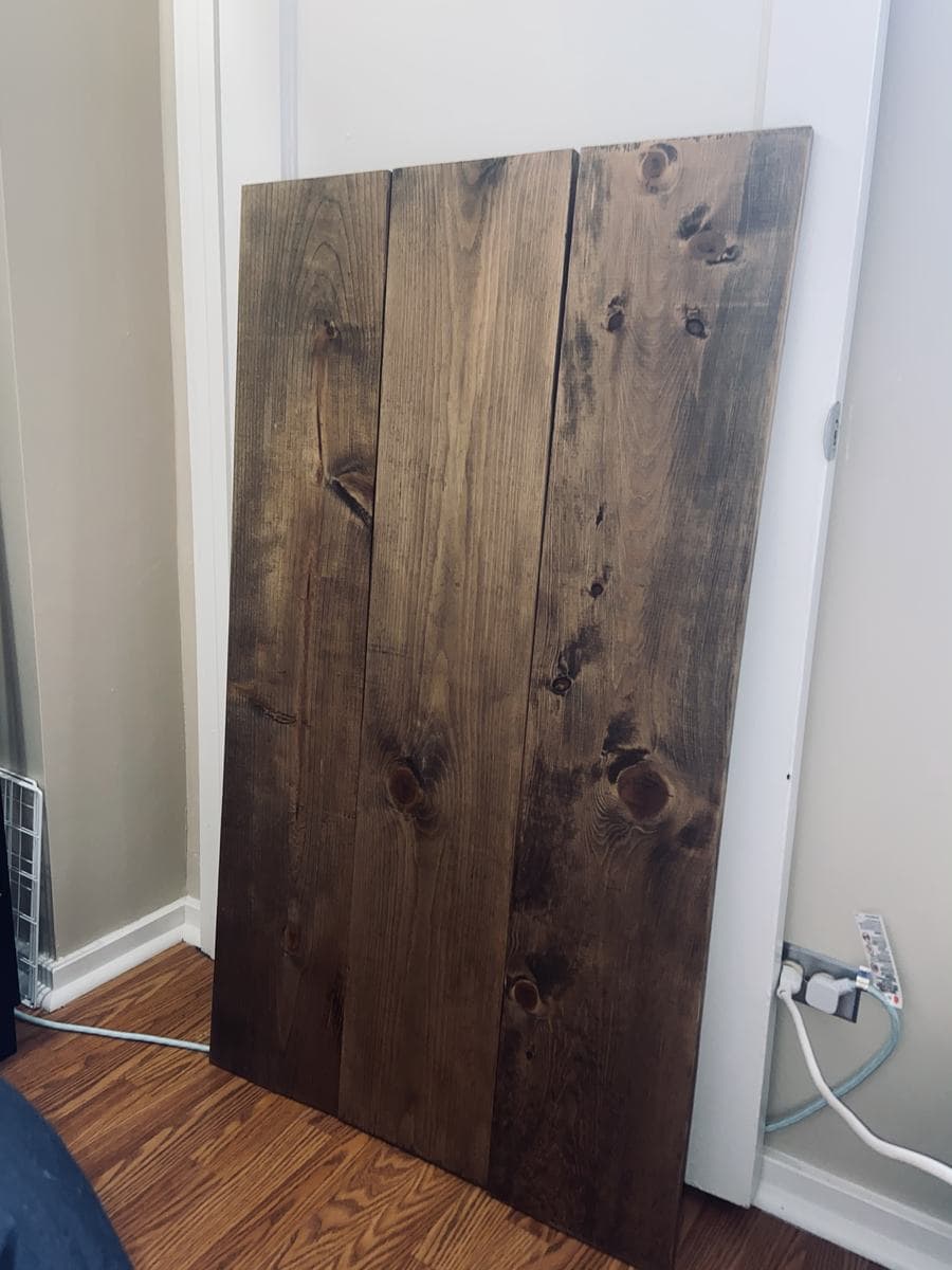Three stained pine boards joined edge to edge, standing upright against a doorframe. The stain is a deep walnut and the grain, knots and one long split read dark against it.