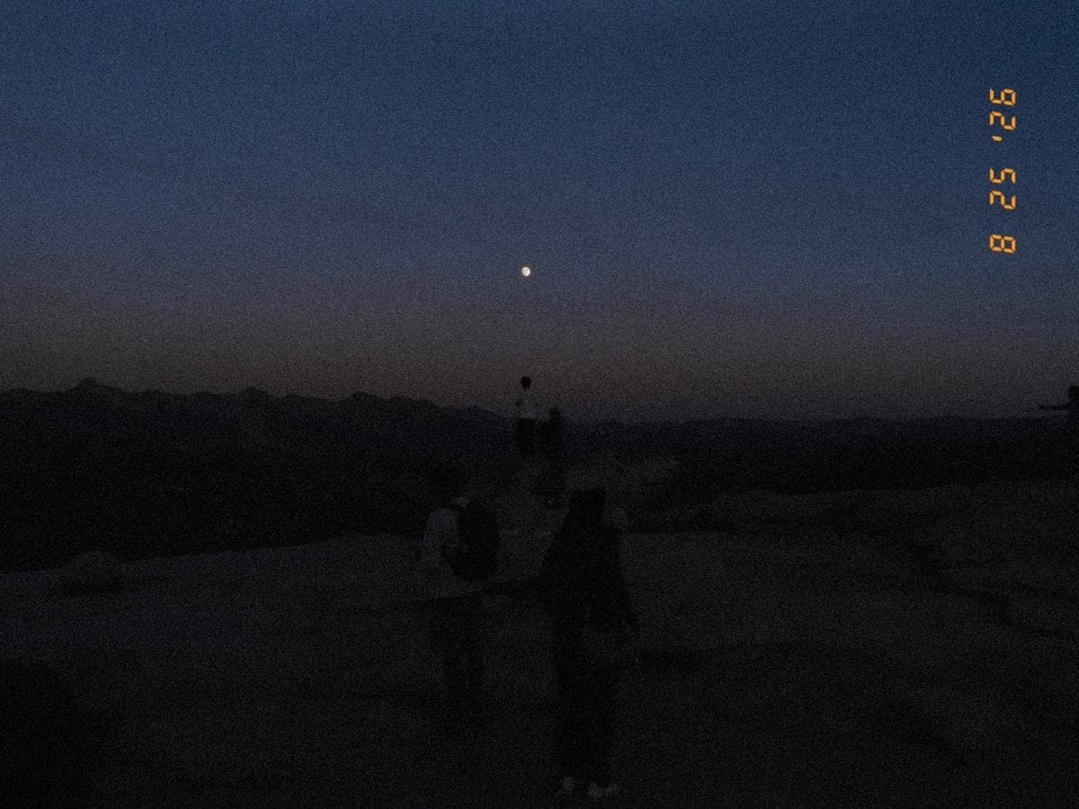 Near dark. Two people stand on bare granite under a sky graded from blue to brown, one point of light above them.